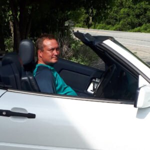 Person driving white convertible car on sunny day.