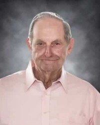 Elderly man smiling in pink shirt.