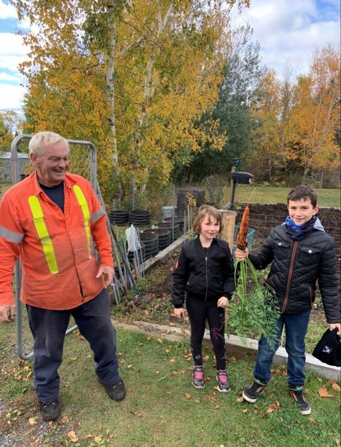 Children proudly show large carrot in garden.