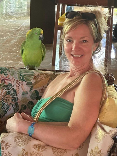 Woman smiling with a green parrot beside her.