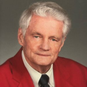 Elderly man in red suit and black tie.
