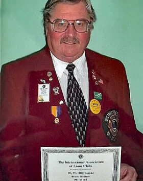 Man holding certificate, wearing red jacket with badges.