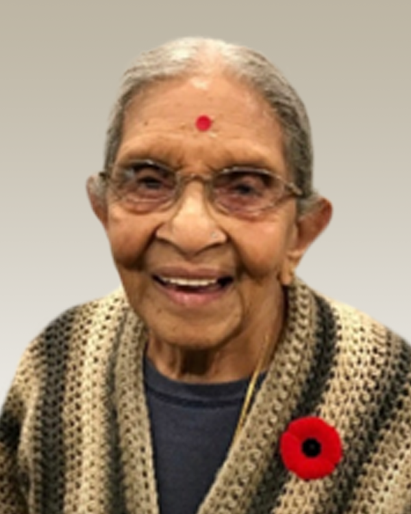 Elderly woman smiling, wearing glasses and a red bindi.