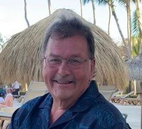 Smiling man outdoors with palm trees in background.