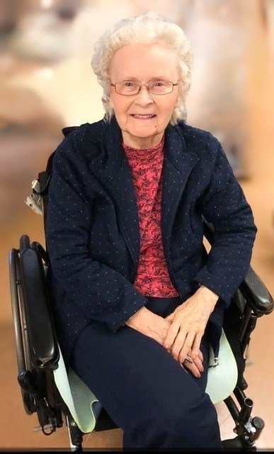 Elderly woman smiling in a wheelchair indoors.