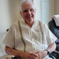 Smiling elderly man sitting indoors wearing casual shirt.