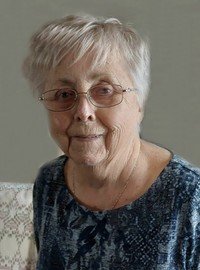 Elderly woman smiling, wearing glasses and blue shirt.