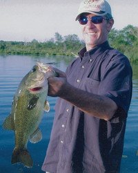 Person holding a large fish by a lake.