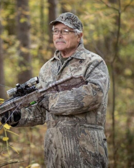 Hunter in camo suit with crossbow in forest.