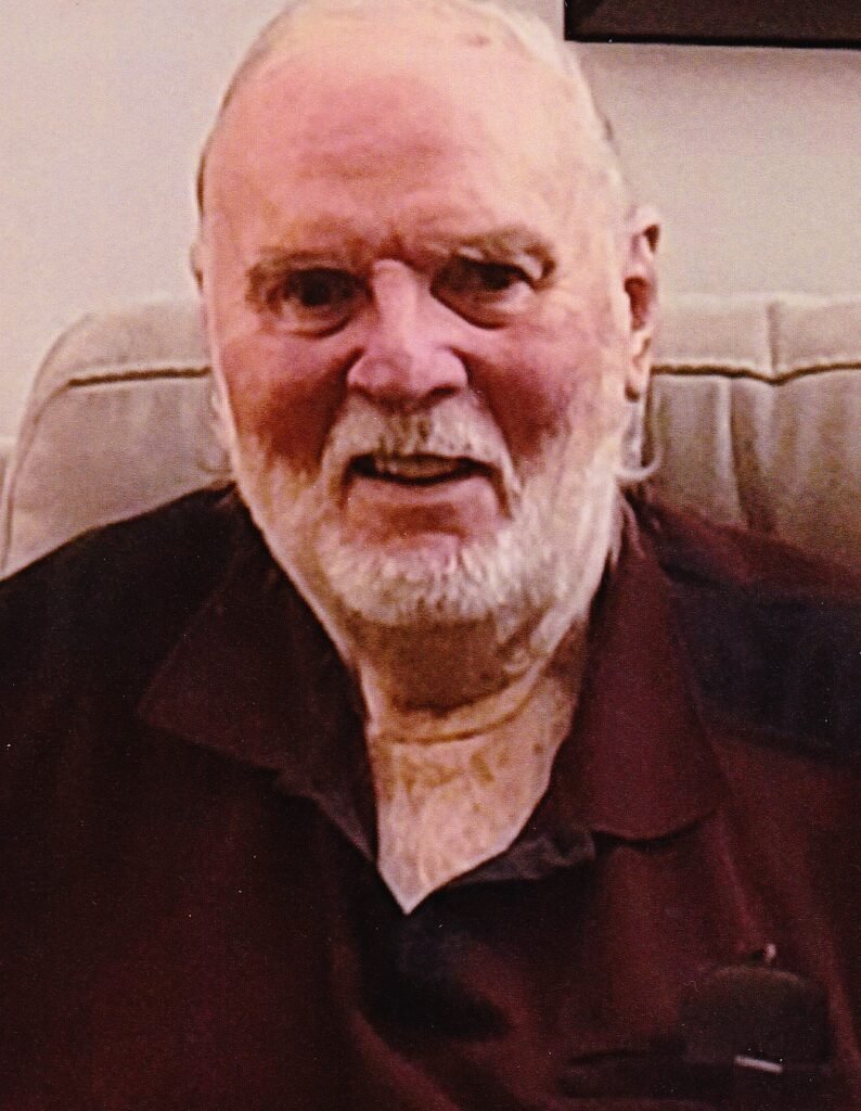 Elderly man sitting on beige couch, smiling.