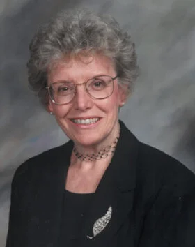 Smiling woman in glasses and suit jacket.