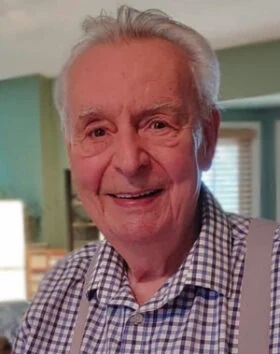 Smiling elderly man in checkered shirt.