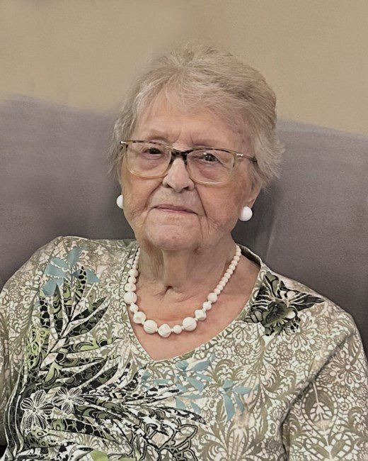 Elderly woman with glasses and floral shirt smiling.