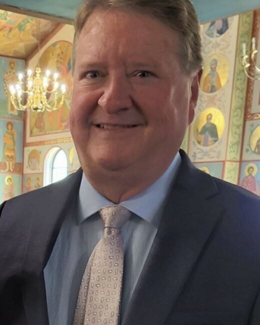 Man smiling in decorated interior, wearing suit and tie.