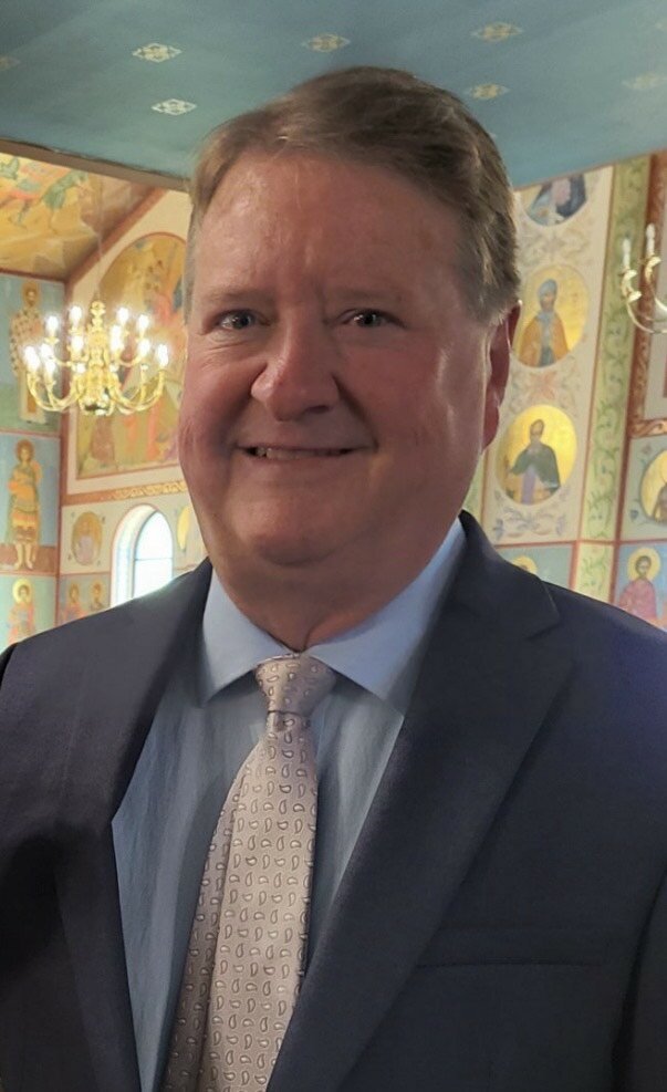 Man smiling in decorated interior, wearing suit and tie.