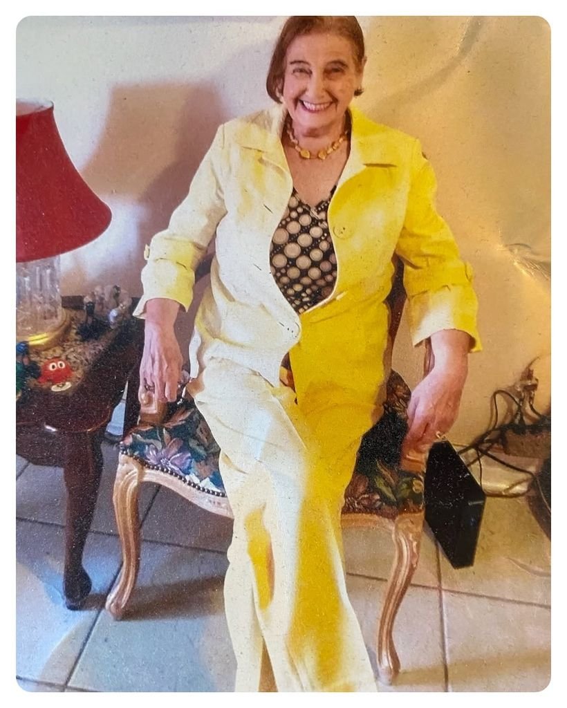 Smiling woman sitting in a yellow suit indoors.
