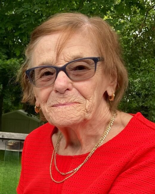Elderly woman in glasses and red top.