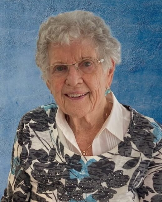 Smiling elderly woman with glasses and floral sweater.