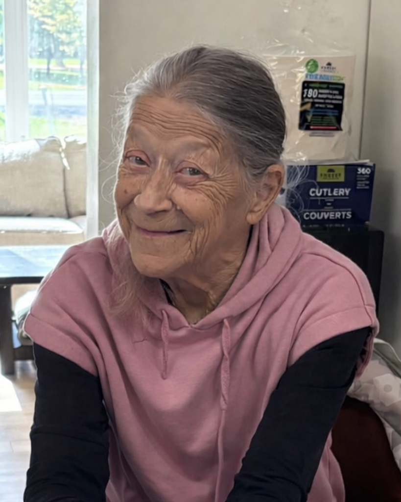 Smiling elderly woman in pink hoodie indoors.