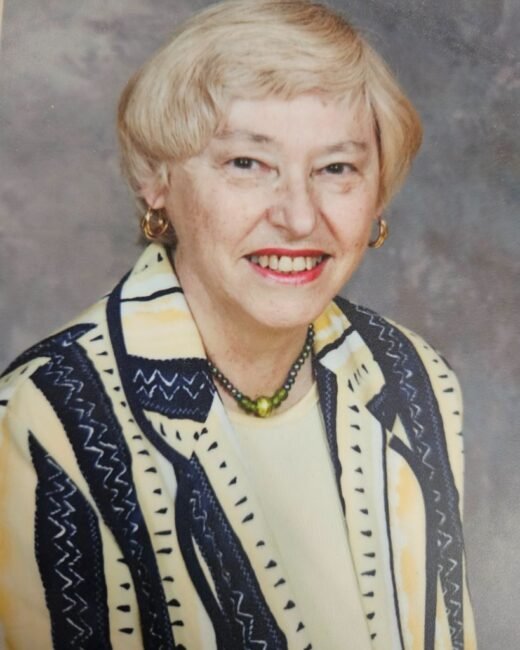 Smiling person wearing patterned jacket and necklace.