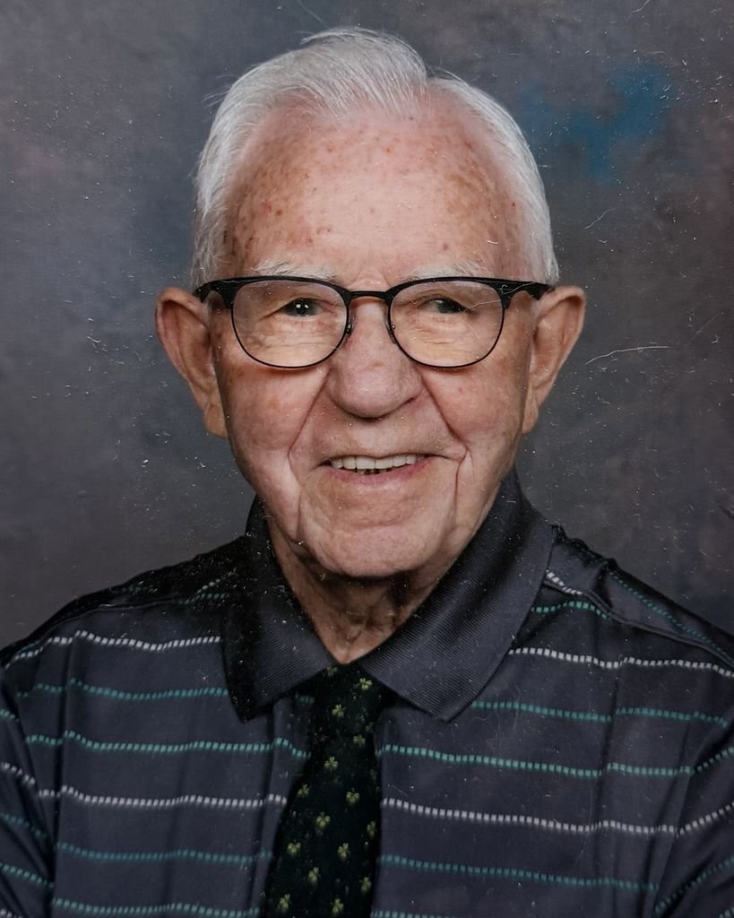 Elderly man smiling in glasses and striped shirt.