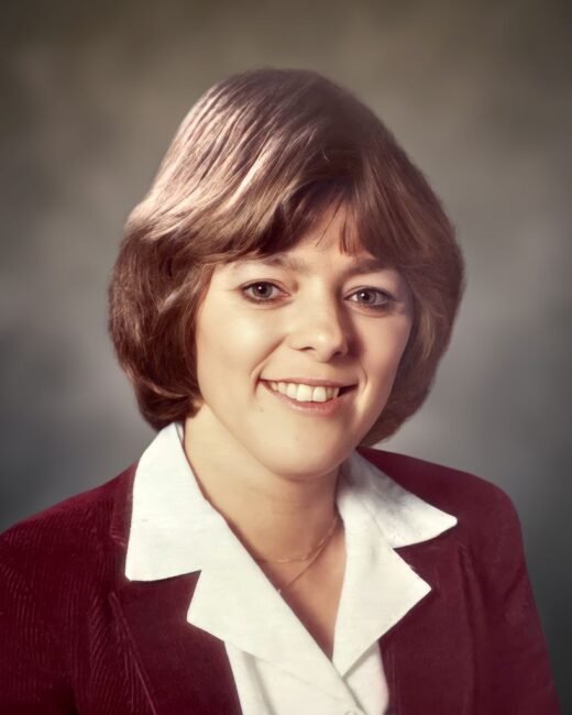 Woman smiling in white shirt and maroon blazer.