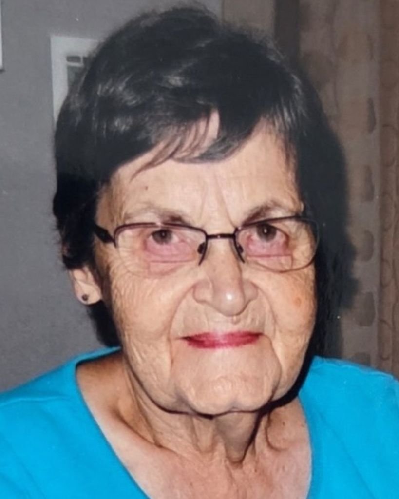 Elderly woman wearing glasses and blue shirt, indoors.