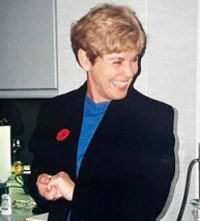 Smiling person in a kitchen wearing a blue shirt.
