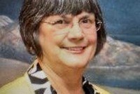 Smiling person with short hair, glasses, scenic background.