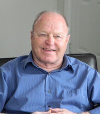 Smiling person sitting indoors in blue shirt.
