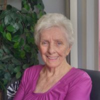 Elderly woman smiling indoors near plants.