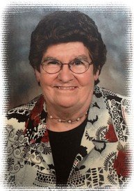 Smiling woman with glasses and patterned blouse.