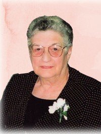 Elderly woman in glasses with white flower corsage.
