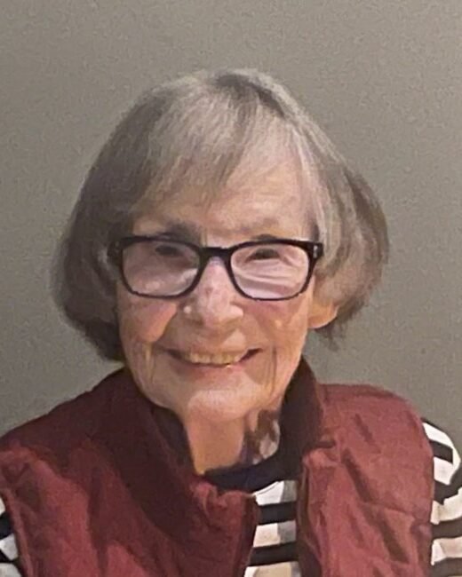 Smiling elderly woman with glasses and striped shirt.