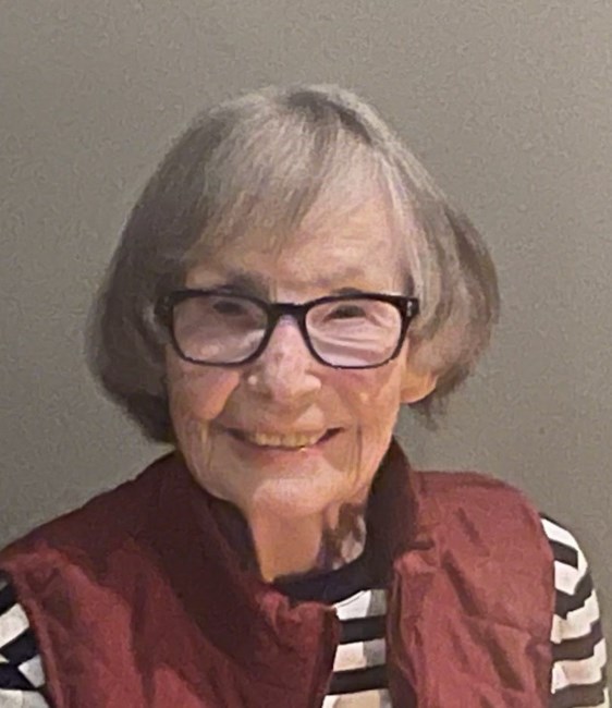 Smiling elderly woman with glasses and striped shirt.