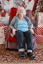 Smiling woman seated, surrounded by holiday decorations.