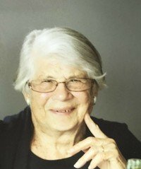 Elderly woman smiling with white hair and glasses.
