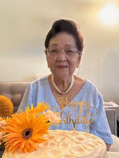 Elderly woman celebrating birthday with cake and flowers.