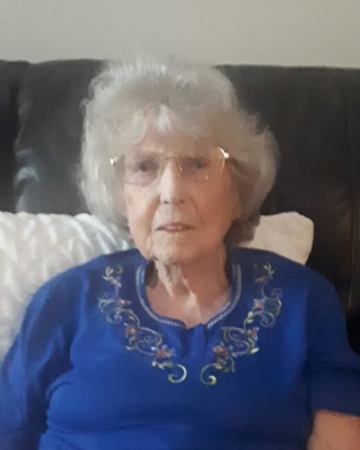 Elderly woman sitting on a couch, wearing glasses.