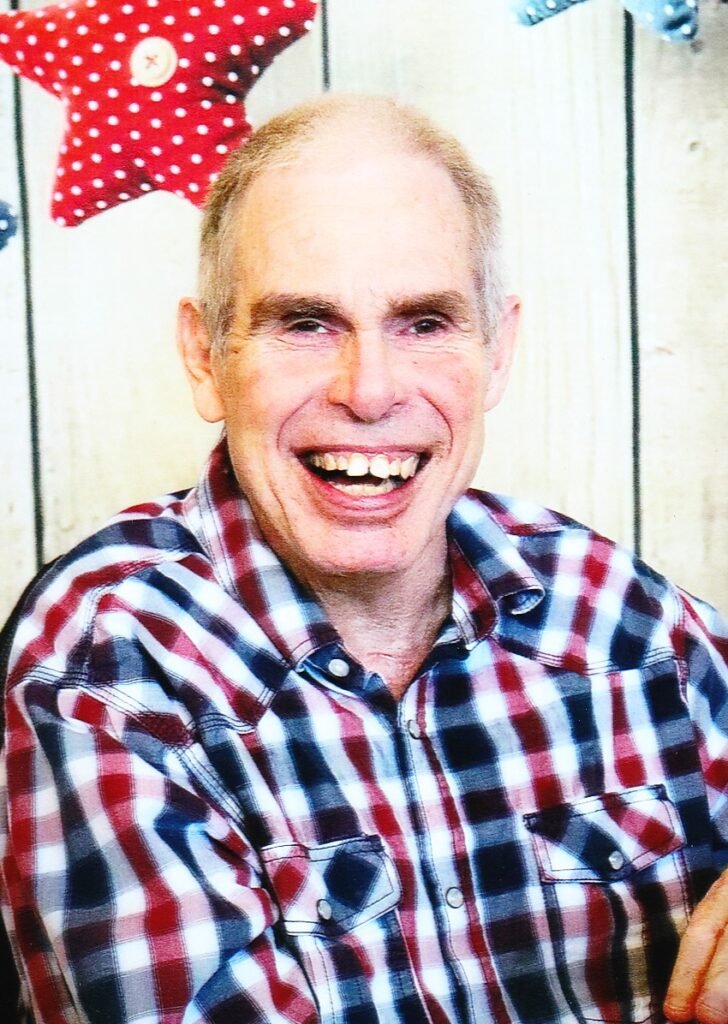 MAHAFFY, Brian Earl Mahaffy Smiling man in checkered shirt with star background.