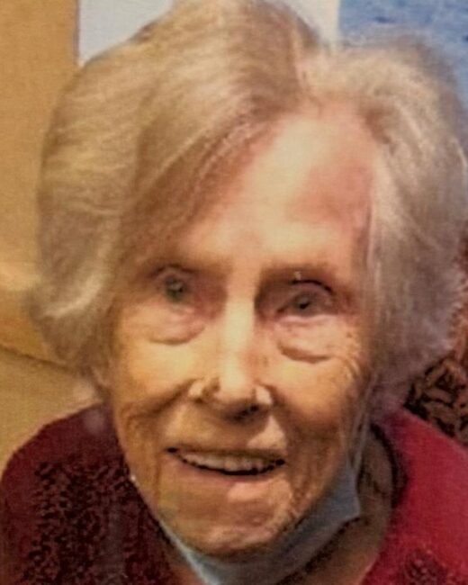 Elderly woman smiling indoors, wearing a face mask.