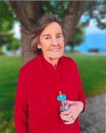 Elderly woman in red, standing outdoors with drink.