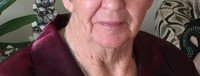 Elderly person smiling in maroon shirt at home.