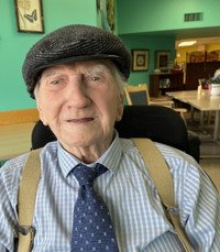 Elderly man smiling in a cafe, wearing cap.