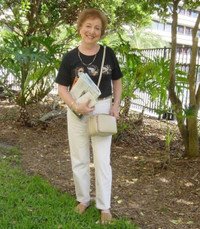 Woman standing outdoors holding a book, smiling.