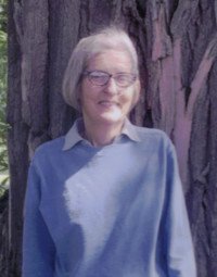 Person smiling in front of large tree trunk.