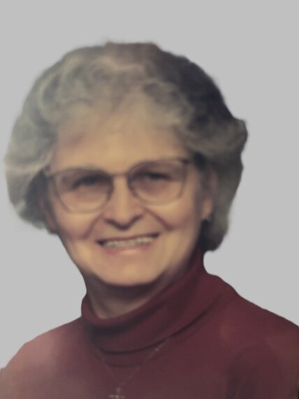 Elderly woman smiling, wearing glasses and a red sweater.