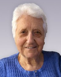 Smiling older woman in blue sweater, white hair.