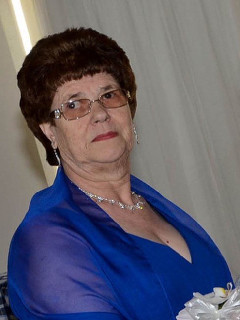 Woman in blue dress with glasses and necklace.