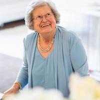 Elderly woman smiling indoors in blue outfit.